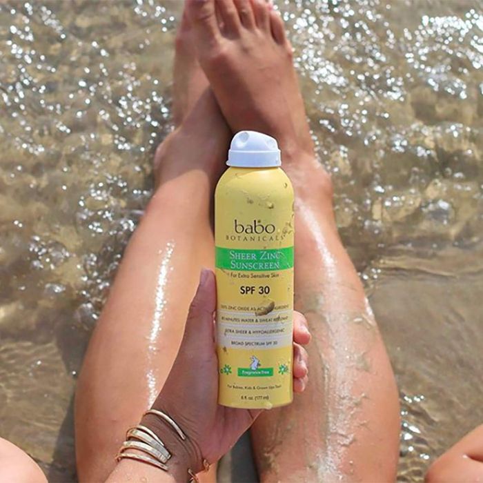 Child applying Babo Botanicals SPF 30 mineral sunscreen spray at the beach