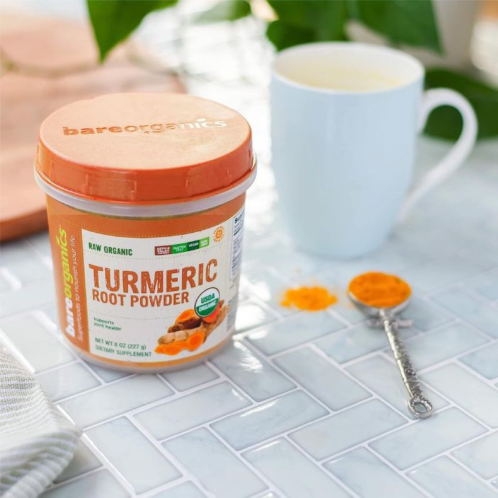 "Scoop of golden turmeric powder in glass jar – vegan and non-GMO"